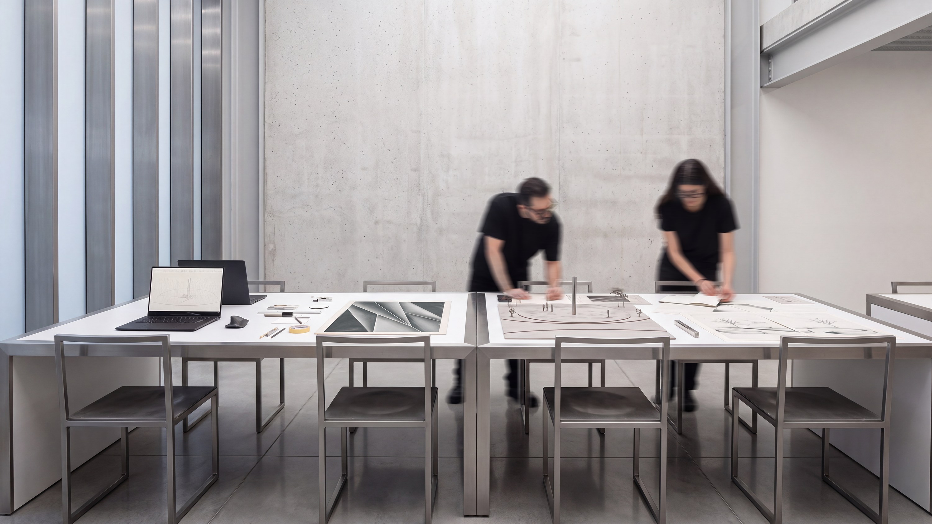 The studio worktable: drawings, a site model, two designers at work