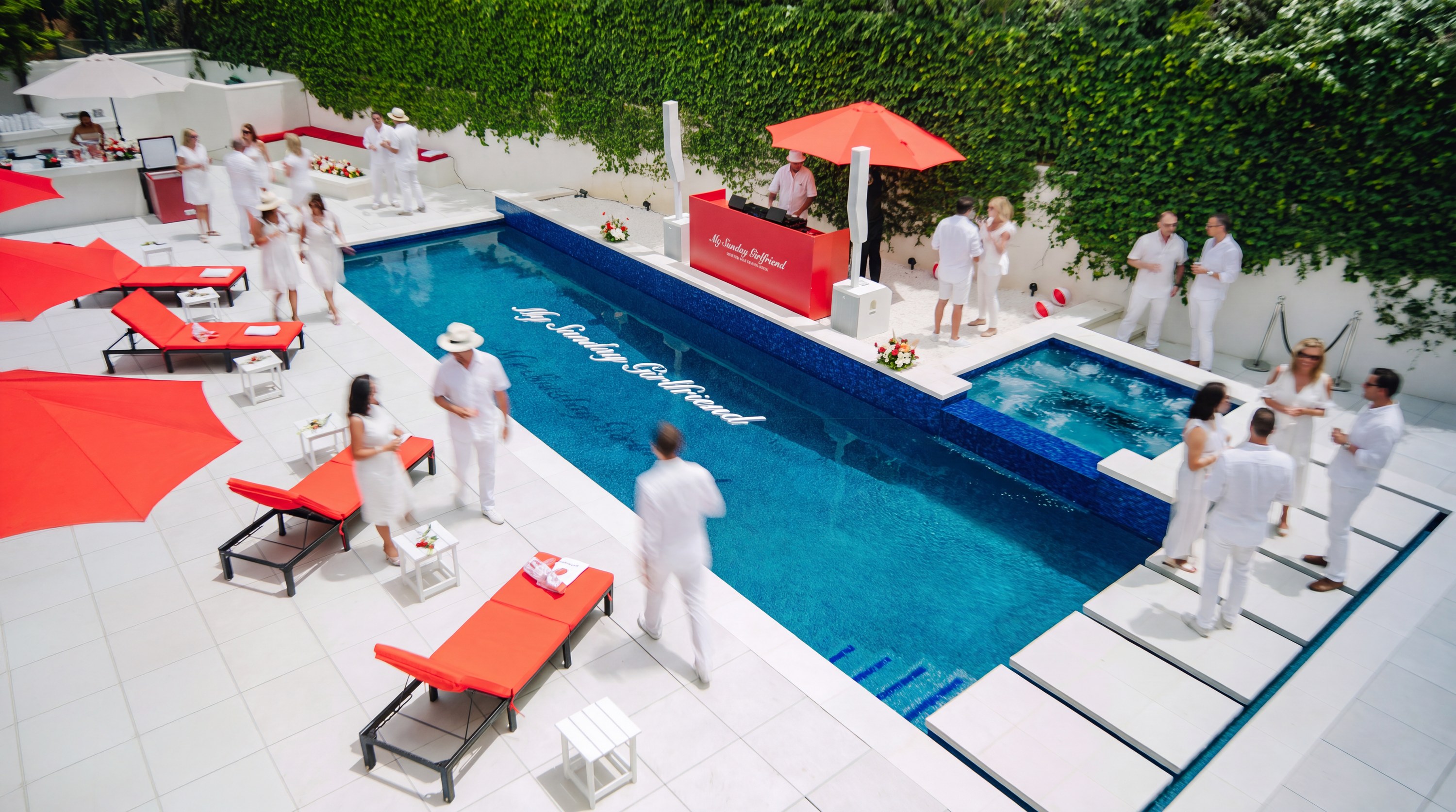 All white pool party with red loungers, umbrellas, and a branded DJ booth